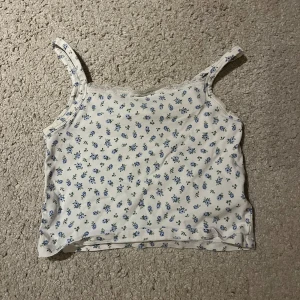 Vit blommig linnetopp från H&M - Söt vit linnetopp från H&M med blått blommönster! Toppen har smala axelband och är perfekt för varma sommardagar. Den är tillverkad i ett mjukt och bekvämt material!!🤗🤗❣️❣️☺️