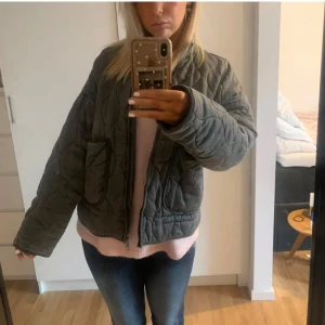 Grå/grön quiltad jacka - Säljer en grå/grön quiltad jacka med dragkedja och långa ärmar. Jackan har en oversized passform och är perfekt för kyligare dagar. Den har en enkel design med praktiska fickor framtill.