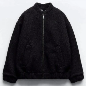 Svart teddyjacka från Zara - Mysig svart teddyjacka från Zara med dragkedja framtill. Jackan har en avslappnad passform och två fickor på sidorna. Perfekt för kyliga dagar!