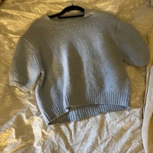 Ljusblå stickad tröja från Zara - Mysig ljusblå stickad tröja från Zara med rund hals och korta ärmar. Perfekt för en avslappnad stil. Tröjan har ribbade kanter vid ärmslut och nederkant.