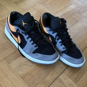 Nike Air Jordans i grått och orange - Säljer ett par Nike Air Jordans i en cool färgkombination av grått, svart och orange. Skorna har klassisk snörning och en ikonisk logga på hälen. De är i okej skick och finns flera tecken på att de har använts en hel del därav säljer jag till ett billigt pris. 