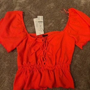 Röd blus med puffärmar - Trendig röd blus från Zara med puffiga kortärmar och knytning framtill. Den har en smickrande passform med elastisk midja och volangdetaljer vid nederkanten. Perfekt för att liva upp garderoben!