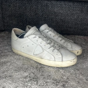 Vita Philippe Model sneakers i skinn - ❗️pris kan diskuteras❗️Snygga vita sneakers från Philippe Model i skinn med klassisk låg profil och rund tå. Skorna har svarta logotyper på snörningen och en beige sula som ger en vintagekänsla. Perfekta för dig som gillar stilrena och tidlösa sneakers.