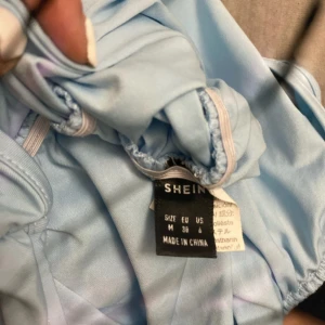 Ljusblå one shoulder klänning SHEIN - Säljer en ljusblå one shoulder klänning från SHEIN i storlek M. Klänningen har en enkel och stilren design med rynkade detaljer längs sidan och är tillverkad i ett mjukt polyestertyg. Perfekt för dig som gillar en modern och fräsch look.