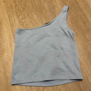 Ljusblå oneshoulder topp Gina Tricot - Säljer en ljusblå ribbad oneshoulder topp från Gina Tricot i storlek S. Toppen har en snygg asymmetrisk design med ett axelband och är tillverkad i mjuk bomull. Perfekt för dig som gillar stilrena och trendiga plagg.