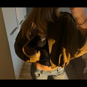 Brun mocka bomberjacka croppad - Säljer en brun croppad bomberjacka i mocka-look med dragkedja framtill och klassisk krage. Jackan har en loose passform och långa ärmar, perfekt för dig som gillar en chill och trendig stil. Enkel design utan mönster eller extra detaljer.