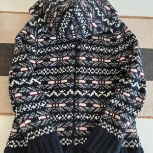 Mönstrad stickad hoodie från Spruce - Säljer en mörkblå stickad hoodie från Spruce med snyggt mönster i vitt, grått och vinrött. Tröjan har huva, dragkedja och breda ribbade muddar. Perfekt för kalla dagar och har en riktigt mysig vibe. Limited edition och riktigt unik design.