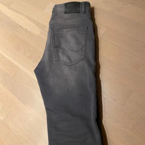 Grå Slim Glenn jeans från Jack and Jones - Snygga grå jeans från Jack and Jones med smal passform och klassisk femficksdesign. Jeansen har en stilren look med en snygg tvätt. Perfekta för dig som gillar en modern och clean stil. Materialet är mjukt och stretchigt för extra komfort.