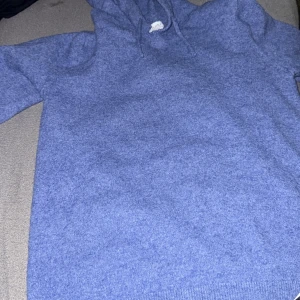 Blå stickad hoodie från Just - Mysig blå hoodie från Just i stickat material. Tröjan har huva med snörning och långa ärmar. Perfekt för dig som gillar chill och enkel stil. Färgen är en snygg mellanmörk blå och materialet känns mjukt och skönt mot huden.