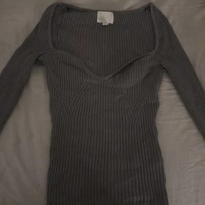  ribbad långärmad tröja - Snygg svart ribbad tröja med lång ärm och markerad byst. Tröjan har en tight passform och är tillverkad i ett stretchigt material som sitter skönt på kroppen. Perfekt för dig som gillar minimalistisk och stilren look.