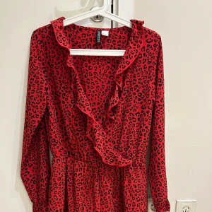  Ny Röd leopardmönstrad klänning H&M - Röd kortklänning från H&M Divided med svart leopardmönster, omlott-look och volangdetaljer längs ringningen. Klänningen har långa ärmar och resår i midjan för en snygg passform. Perfekt för dig som vill sticka ut med en djärv stil. Det är som en S i Stl 