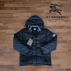 Burberry Puffer - Svart dunjacka från Burberry med klassisk Säljer en elegant och mångsidig Burberry-jacka i svart, i nyskick. Dunfodrad för värme och komfort med det klassiska rutmönstret i huvan som ger en exklusiv touch. Praktiska dragkedjefickor, avtagbar huva och diskret logopatch på ärmen. Jackan är i princip som ny och utan defekter. En lyxig kombination av stil och funktion – perfekt för både vardag och tillfällen då du vill klä upp dig.  📦Snabb leverans - skickas samma dag📌