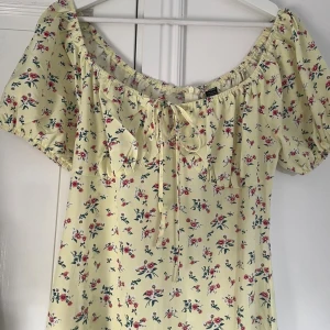 Gul blommig långklänning med snörning - Söt långklänning från shein i ljusgul nyans med små rosa och vita blommor. Klänningen har korta puffärmar, snörning vid bysten.