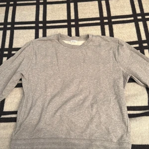 Grå sweatshirt från Filippa K - En stilren grå sweatshirt från Filippa K i klassisk modell. Tröjan har rund halsringning, långa ärmar och är tillverkad i mjuk bomullsmix. Perfekt för en avslappnad och clean look.