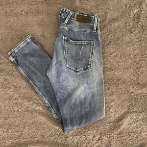 Replay Anbass slim jeans blå - Säljer ett par Replay Anbass slim jeans i blå tvätt med slitningar och snygga detaljer. Jeansen har klassisk femficksdesign, låg midja och smal passform. Materialet är stretchigt jeans för en bekväm känsla. Perfekta för dig som gillar en modern och avslappnad look.