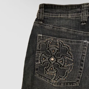 Svart jeanskjol med broderade fickor - Cool svart jeanskjol från Rock & Republic med snygga broderade detaljer och nitar på bakfickorna. Klassisk femficksmodell med bälteshällor och knappstängning. Minikjol i jeans typ i väldigt bra skick