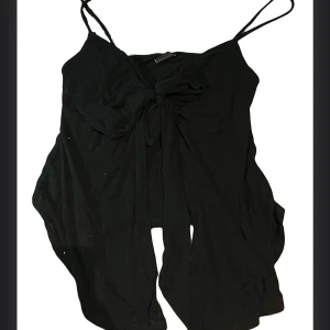 Svart linnetopp med knyt från Gina Tricot - Säljer en svart linnetopp från Gina Tricot i storlek M. Toppen har tunna axelband och en snygg knytning framtill som ger en cool och trendig look. Perfekt för varma dagar eller att styla lager på lager.