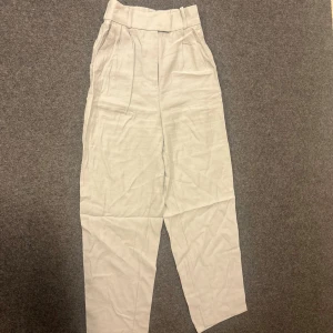 Beiga högmidjade linnebyxor - Snygga beiga linnebyxor med hög midja och avslappnad passform. Byxorna har bred linning, veck framtill och raka ben. Perfekta för en chill och stilren look.