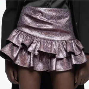 Glittrig volangkjol från Zara - Säljer en glittrig kortkjol från Zara i mörklila med metallicskimmer. Kjolen har två lager volanger som ger extra flärd och en figurnära passform i midjan. Perfekt för dig som vill sticka ut med en cool och trendig look. Kjolen är i storlek M, men passar mig bra som har storlek S💖