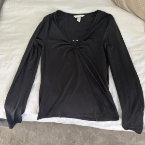 Svart långärmad topp från H&M - Svart långärmad topp från H&M med v-ringning och snygg rynkdetalj framtill som skapar en liten cut-out. Toppens material är stretchigt och följsamt, vilket ger en tight passform. Perfekt att styla med jeans eller kjol för en trendig look. Pris kan diskuteras!!!!