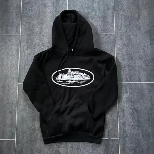 Svart hoodie - Svart hoodie med stor huva och snörning. Tröjan har en klassisk känguruficka framtill och ribbade muddar vid ärmslut och nederkant. Perfekt för chill dagar och streetstyle.