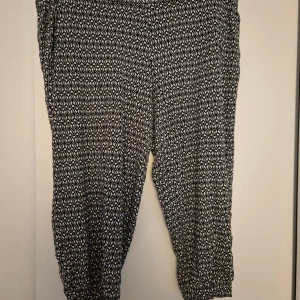 Svartvita mönstrade byxor Cubus XL - Svartvita byxor från Cubus i storlek XL med grafiskt mönster. Tillverkade i mjuk och stretchig viskosblandning som gör dem riktigt sköna. Perfekta för dig som gillar bekväma och snygga byxor med lite loose fit.