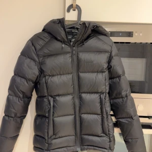 Svart dunjacka  från Everest - W Expedition Down Jacket från Everest är en varm och funktionell dunjacka för kyliga vinterdagar. Den är vadderad med 90/10 dun och har en fillpower på 650, vilket ger en puffig känsla och pålitlig värme utan att jackan känns tung   Utfällbar reflekterande detalj i fickan  Dragsko i nederkanten för justerbar passform 90% dun och 10% fjäder (650 fillpower)  Använd ett fåtal gånger så den är i nyskick.  Nypris 2500kr