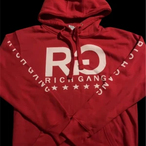Rich Gang Hoodie - Säljer en röd Rich Gang Hoodie (custommade) med stort vitt tryck på bröstet och text längs ärmarna. 
