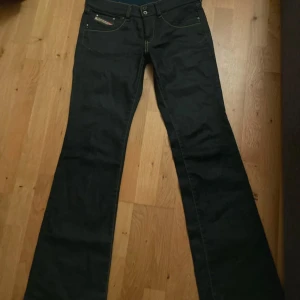 Svarta bootcut jeans Diesel - Snygga svarta jeans från Diesel med bootcut passform. Klassisk femficksmodell med diskreta sömmar och logga på myntfickan. Jeansen har låg midja och är tillverkade i ett mjukt bomullsmaterial med lite stretch för extra komfort. 37cm i midja.