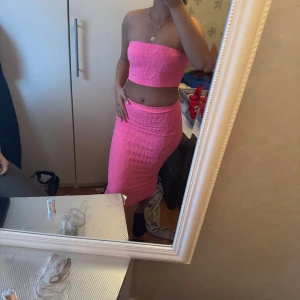 Rosa set - Säljer en snygg midilång kjol,topp/ sett  i starkt rosa färg. Kjolen är figurnära och har ett vågigt strukturmönster i tyget. Den är högmidjad och gjord i ett stretchigt material som sitter tajt och markerar formerna. Perfekt för dig som vill sticka ut med en färgglad look. Toppen är super snygg och passar fint
