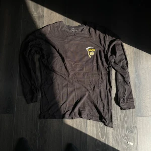 Svart långärmad Vans tröja - Svart långärmad tröja från Vans med coolt tryck på ryggen och liten logga på bröstet. Skön passform och tillverkad i mjuk bomull. Perfekt för dig som gillar streetwear och vill sticka ut med en unik design.