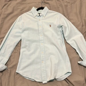 Ljusblå skjorta Polo Ralph Lauren S - Klassisk ljusblå skjorta från Polo Ralph Lauren i slim fit-modell. Skjortan har button down-krage, broderad logga på bröstet och är tillverkad i stretchig bomull. Perfekt för en clean och stilren look.