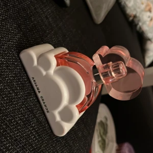 Ariana Grande parfym rosa flaska - Snygg parfym från Ariana Grande i en unik rosa flaska med moln-detaljer. Perfekt för dig som vill sticka ut och addera en poppig touch till din samling.  30ml om man vill prova på denna doft, halva kvar i. 