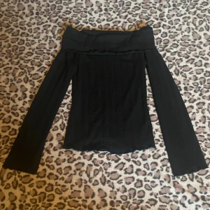 Svart offshoulder tröja - Svart offshoulder topp i ribbat material med diskret mönster. Långa ärmar, perfekt för att skapa en snygg och trendig look. Endast testad.