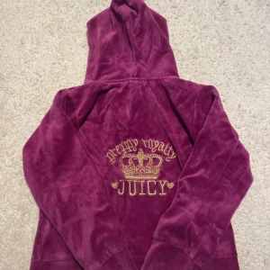 Vintage Juicy Couture - Juicy Couture hoodie i lila velour med guldbroderad krona och texten 'preppy royalty JUICY' på ryggen. Dragkedja framtill, huva och kängurufickor. Den är en barn xxl villket som är typ en xxxxs i vuxen storlek. Ikonisk Y2K-stil som är supermysig och perfekt för chill dagar. 