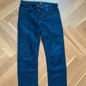 Mörkblå Lee jeans W29 L32 - Snygga mörkblå jeans från Lee med klassisk straight fit och fem fickor. Jeansen har kontrastsömmar, knappgylf och Lee-logga på bakfickan. Perfekt för dig som gillar tidlös stil och vill ha ett par jeans som funkar till allt. W29 L32 nyskick