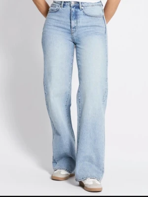 Ljusblå wide jeans med hög midja - Säljer ett par ljusblå jeans från Lager 157 med hög midja och breda ben. Klassisk femficksmodell med knapp och dragkedja framtill. Jeansen är tillverkade i jeansmaterial och har en avslappnad, loose passform som ger en chill vibe. Helt nya ich oanvänd