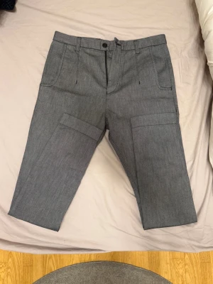 Hugo Boss byxor - Snygga grå byxor från Hugo Boss med raka ben och praktiska fickor på sidorna. Byxorna har midwaist och är tillverkade i bomullsmaterial. Passar dig som gillar stilrena och funktionella plagg med modern touch. Se bild för exakt storlek. Vid funderingar eller liknande är det bara att höra av sig! 
