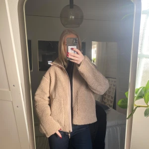 Beige teddyjacka med dragkedja - Mysig beige teddyjacka med hög krage och dragkedja framtill. Jackan har två stora fickor på framsidan och en loose passform. Tjockare i materialet och perfekt till vintern. Storlek 170 men skulle säga att den är som storlek Xs/S. Från hm.