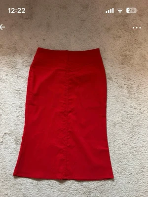 Röd midikjol  - Säljer en röd midikjol knapp framtill i midjan. Kjolen är tillverkad av mjukt material med stretch, innehåller viskos, nylon och elastan. Enkel och stilren design som är lätt att matcha med olika toppar. Fin julkjol