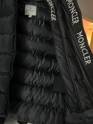 Svart Moncler pufferjacka med huva - Säljer en svart pufferjacka från Moncler i storlek S. Jackan har huva, dragkedja framtill och Moncler-logga på insidan av kragen. Den är quiltad och har två sidofickor med dragkedja. Perfekt för dig som vill ha en stilren och varm jacka.