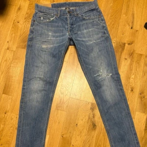 Dondup Jeans - Säljer ett par blå Dondup jeans med skinny passform och slitna detaljer på benet och vid midjan. Jeansen har klassiska fem fickor och är gjorda i jeansmaterial med en tvättad look. Perfekt för dig som gillar en avslappnad och trendig stil.