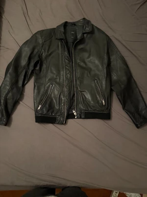 Svart skinnjacka från Emilio  - Snygg svart skinnjacka från Emilio med klassisk krage och två dragkedjeförsedda fickor framtill. Jackan har långa ärmar och en stilren look med silverfärgade detaljer. Perfekt för dig som vill ha en cool och tidlös jacka.