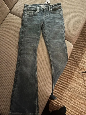 Ultra low bootcut jeans från gina trcot  - Säljer ett par blå ultra low bootcut jeans från Gina tricot, med snygga kontrastsömmar på bakfickorna och klassisk. Perfekt för dig som gillar retrovibbar och markerad siluett.