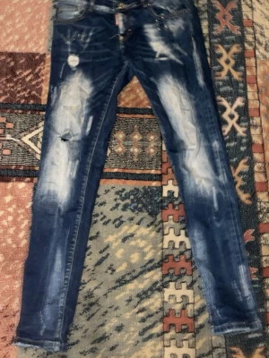 Blå skinny jeans med slitningar - Säljer ett par blå skinny jeans med coola slitningar och blekta detaljer på benen. Jeansen har klassisk femficksdesign och smal passform som sitter tajt längs benen. Perfekt för dig som gillar en edgy streetstil.