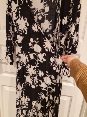 Svartvit omlottklänning Johanna Ortiz x H&M - Säljer en lång svartvit omlottklänning från Johanna Ortiz x H&M i storlek M. Klänningen har blommigt mönster, trekvartsärm och knyt i midjan. Tillverkad i 100% viskos för ett mjukt och följsamt fall. Perfekt för dig som gillar statement-plagg!