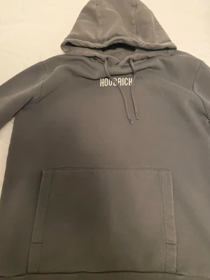 Mörkgrå tracksuit från Hoodrich - Säljer ett par mörkgrå mjukisbyxor från Hoodrich med vit logotyp på vänster lår. Byxorna har snörning i midjan, muddar vid bensluten och är gjorda i mjukt bomullsmaterial. Perfekta för chill eller streetwear-stil.