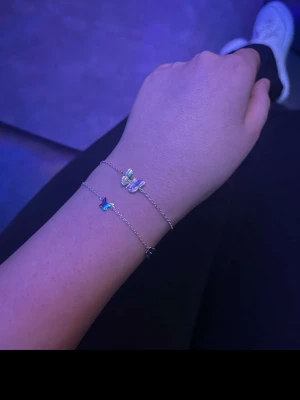 Silvrig fjärilsarmband i tunn kedja - Säljer ett tunt och stilrent armband i silverfärgad metall med små fjärilar som detaljer. Kedjan är smal och har en elegant look, perfekt för dig som gillar subtila smycken med en twist. Fjärilarna ger armbandet en söt och trendig vibe.