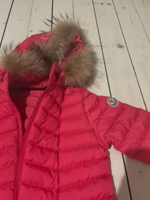 Rosa Moncler dunjacka med päls - Säljer en röd dunjacka från Moncler med fluffig päls på huvan och snygga quiltade detaljer. Jackan har dragkedja framtill, två fickor med dragkedja och Moncler-logga på ärmen. Perfekt för dig som vill ha en varm och stilren look. Vet inte om det är äkta eller inte . Sprillans ny , pris kan diskuetaras .