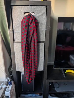 Svart väst med röda prickar - Säljer en svart väst med röda prickar som ger en cool och lekfull vibe. Västen har en rak form och är tillverkad i ett mjukt tyg, troligtvis polyester. Perfekt för dig som vill sticka ut med ett färgstarkt mönster.